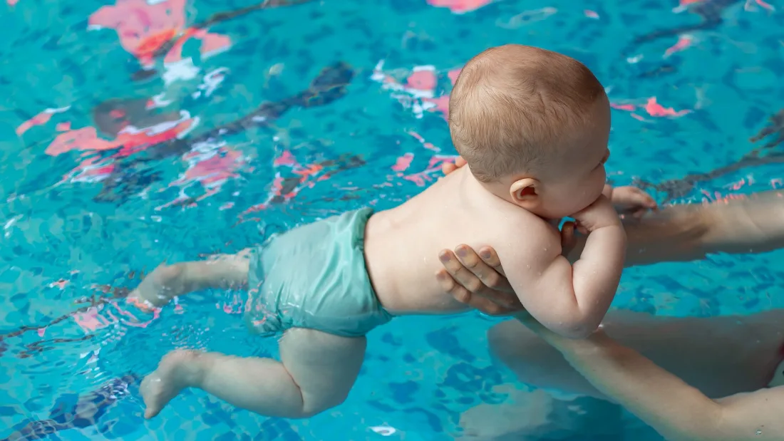 Baby im Wasser, gehalten von einer Begleitperson